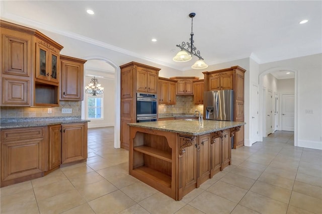 kitchen featuring tasteful backsplash, hanging light fixtures, a kitchen island with sink, stainless steel appliances, and light stone countertops