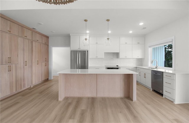 kitchen with white cabinets, light hardwood / wood-style flooring, a kitchen island, and appliances with stainless steel finishes