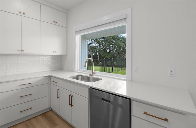 kitchen with stainless steel dishwasher, backsplash, white cabinetry, and sink