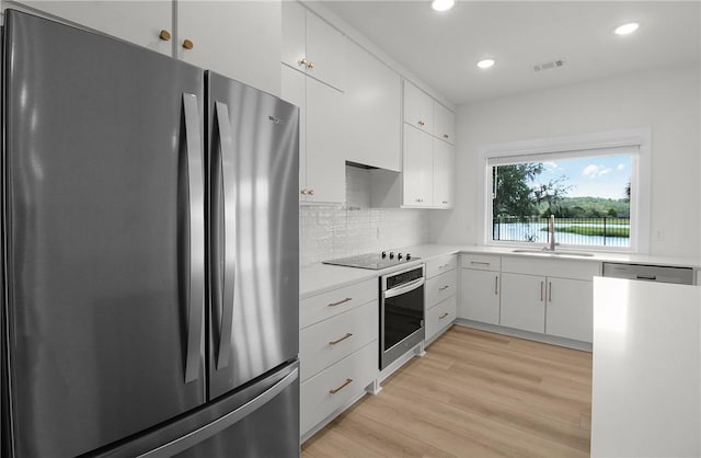 kitchen with backsplash, white cabinets, sink, light hardwood / wood-style flooring, and stainless steel appliances