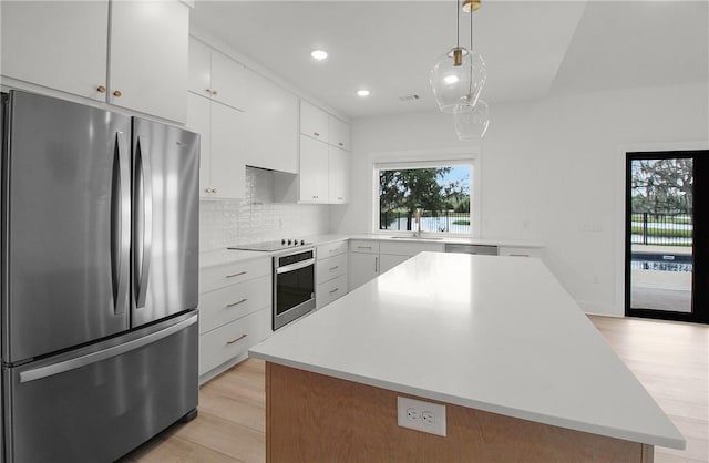 kitchen featuring a center island, appliances with stainless steel finishes, pendant lighting, white cabinets, and light wood-type flooring