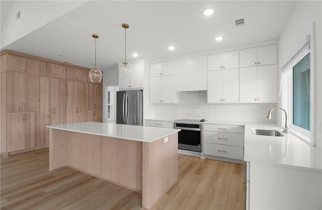 kitchen with stainless steel appliances, a kitchen island, white cabinetry, and light hardwood / wood-style floors