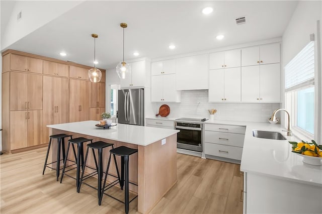 kitchen with appliances with stainless steel finishes, pendant lighting, white cabinets, a center island, and light hardwood / wood-style floors