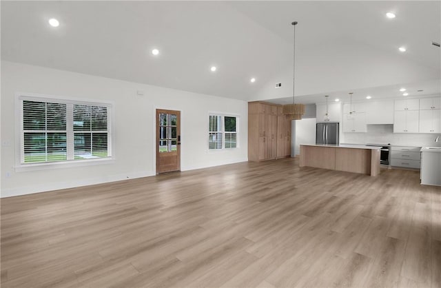 unfurnished living room featuring light wood-type flooring, sink, and high vaulted ceiling