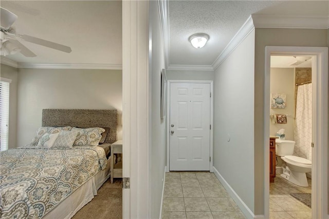 bedroom featuring baseboards, ornamental molding, light tile patterned floors, ensuite bathroom, and a textured ceiling