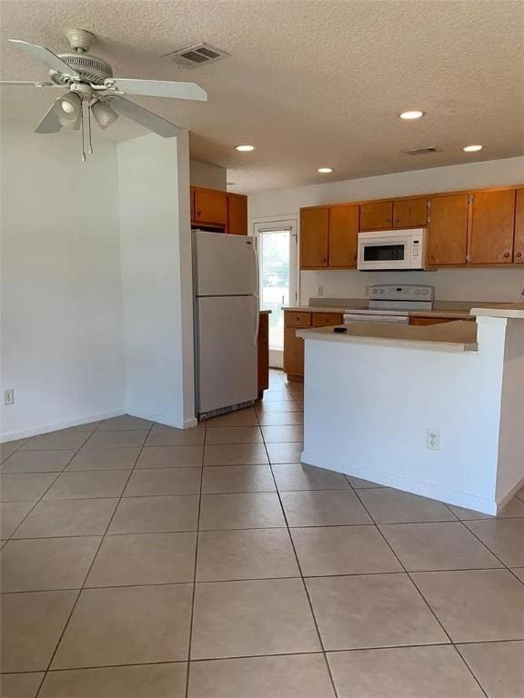 kitchen with a textured ceiling, white appliances, and light tile patterned flooring