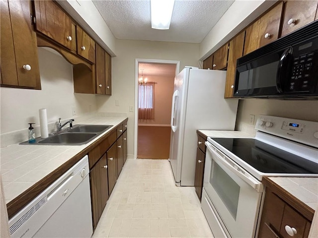 kitchen featuring a notable chandelier, a sink, a textured ceiling, tile countertops, and white appliances