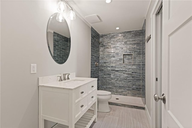 bathroom with tiled shower, tile patterned flooring, vanity, and toilet