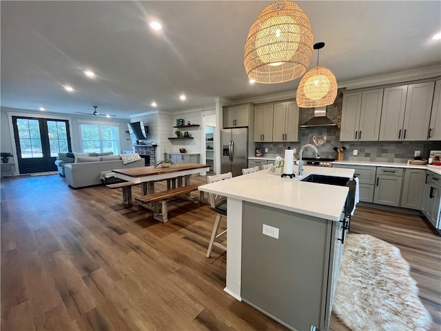 kitchen with dark wood-style flooring, light countertops, gray cabinetry, wall chimney range hood, and stainless steel fridge