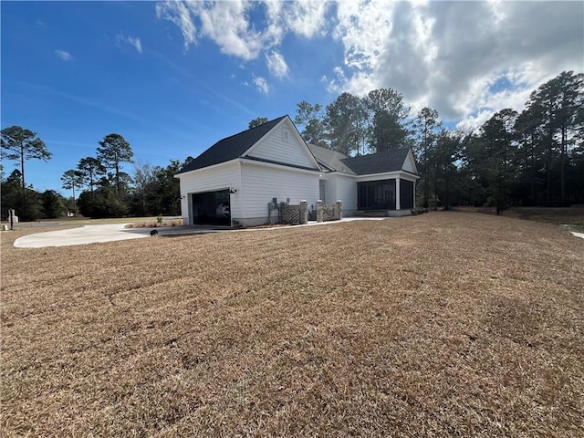 view of home's exterior with a garage, a sunroom, driveway, and a lawn