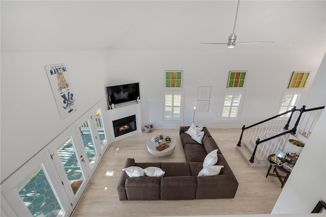 living room with a high ceiling, ceiling fan, wood finished floors, a lit fireplace, and stairs