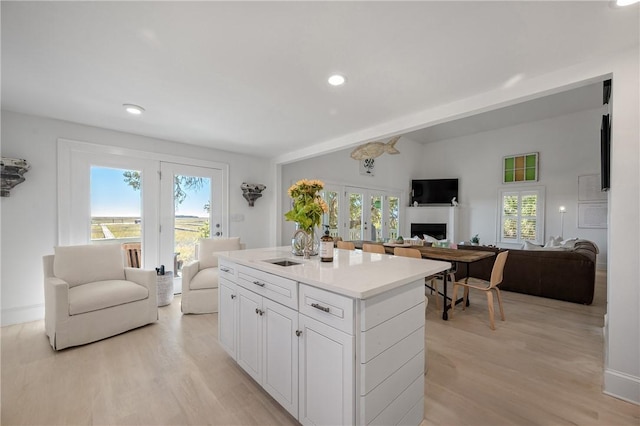 kitchen featuring a fireplace, a kitchen island, a sink, open floor plan, and light wood finished floors