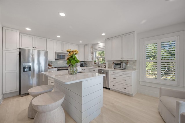 kitchen with tasteful backsplash, appliances with stainless steel finishes, light countertops, light wood-type flooring, and white cabinetry