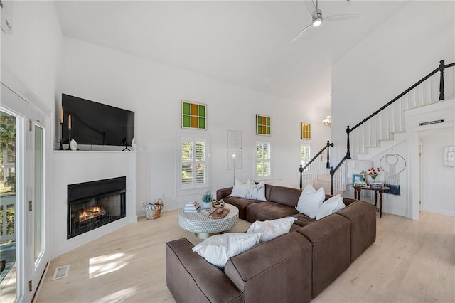 living room featuring a towering ceiling, light wood-style floors, stairway, and a glass covered fireplace