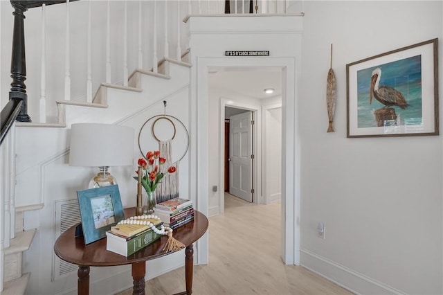 hall with light wood finished floors, baseboards, and stairway