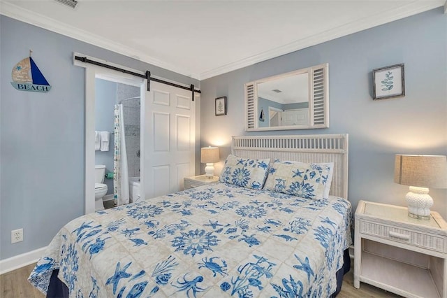 bedroom with hardwood / wood-style flooring, a barn door, crown molding, and ensuite bath