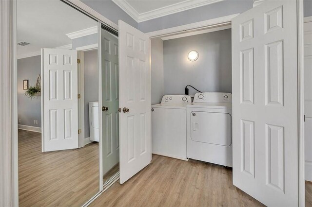 clothes washing area with washing machine and clothes dryer, crown molding, and light hardwood / wood-style floors