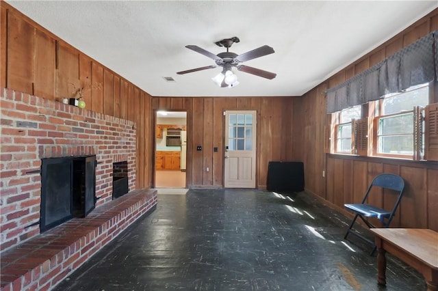 unfurnished living room featuring ceiling fan, wood walls, a brick fireplace, and visible vents