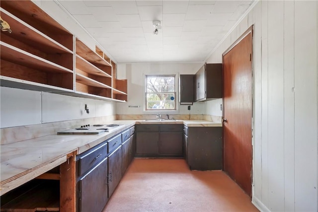 kitchen with white stovetop, light countertops, dark brown cabinets, open shelves, and a sink