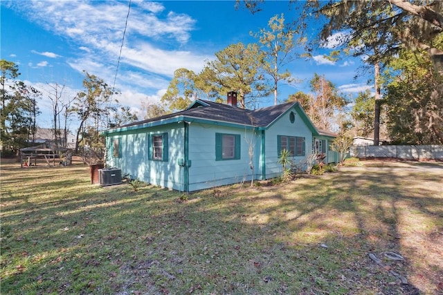 view of side of property featuring a chimney, fence, central AC unit, and a yard