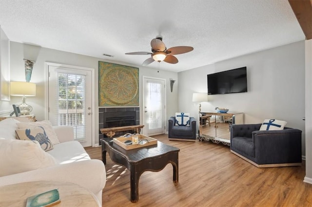 living room with hardwood / wood-style flooring, ceiling fan, a fireplace, and a textured ceiling