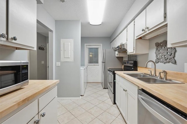 kitchen featuring appliances with stainless steel finishes, sink, washing machine and clothes dryer, white cabinetry, and light tile patterned flooring