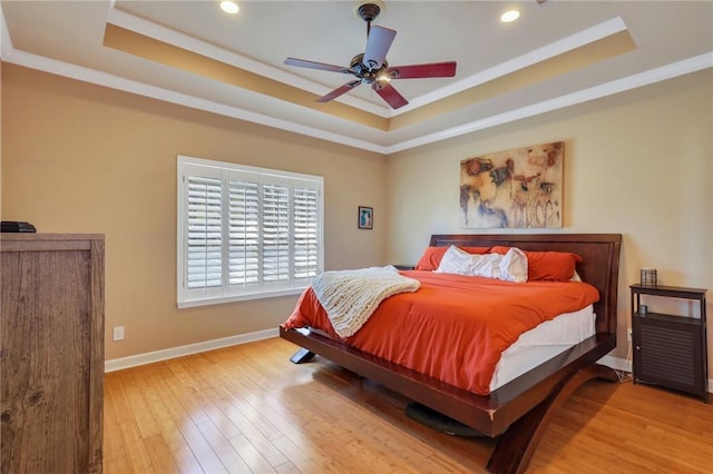 bedroom with ceiling fan, a tray ceiling, and light wood-type flooring