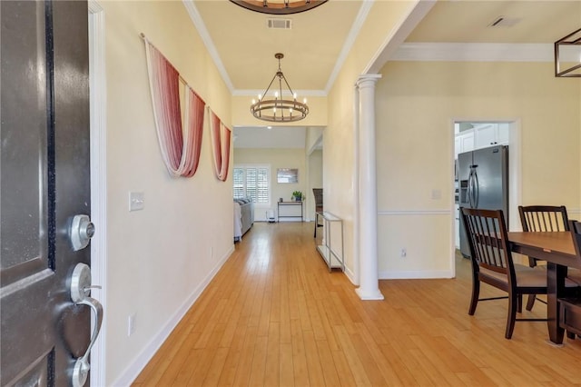 foyer featuring a notable chandelier, light wood-type flooring, ornamental molding, and ornate columns