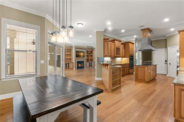 kitchen with a peninsula, a lit fireplace, ventilation hood, dark stone countertops, and decorative light fixtures