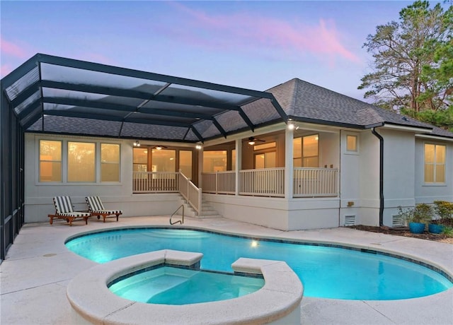 back of property at dusk with roof with shingles, a patio, a pool with connected hot tub, a ceiling fan, and a lanai