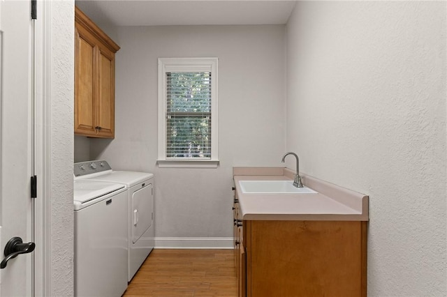 clothes washing area with cabinet space, baseboards, light wood-style floors, washing machine and dryer, and a sink