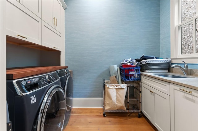 laundry room with washing machine and clothes dryer, sink, cabinets, and light wood-type flooring