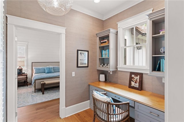 office area featuring light wood-type flooring, built in desk, and crown molding