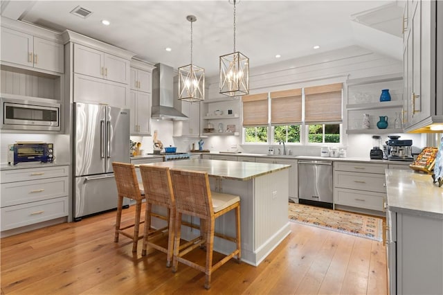 kitchen with a kitchen breakfast bar, wall chimney range hood, a kitchen island, light hardwood / wood-style floors, and stainless steel appliances