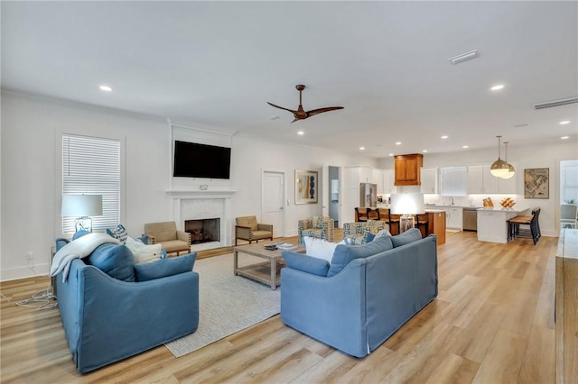 living room featuring a high end fireplace, light hardwood / wood-style floors, and ceiling fan