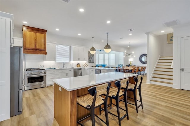 kitchen with white cabinetry, decorative light fixtures, a kitchen bar, a kitchen island, and appliances with stainless steel finishes