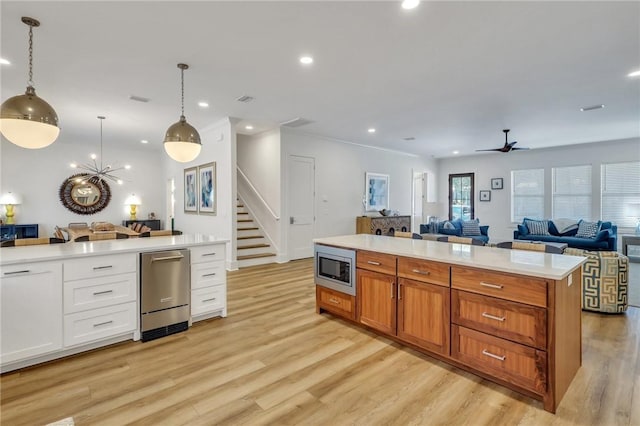 kitchen with white cabinets, ceiling fan with notable chandelier, hanging light fixtures, light wood-type flooring, and appliances with stainless steel finishes