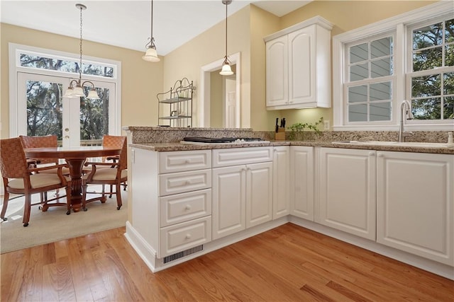 kitchen featuring white cabinets, hanging light fixtures, light wood-type flooring, gas cooktop, and a sink