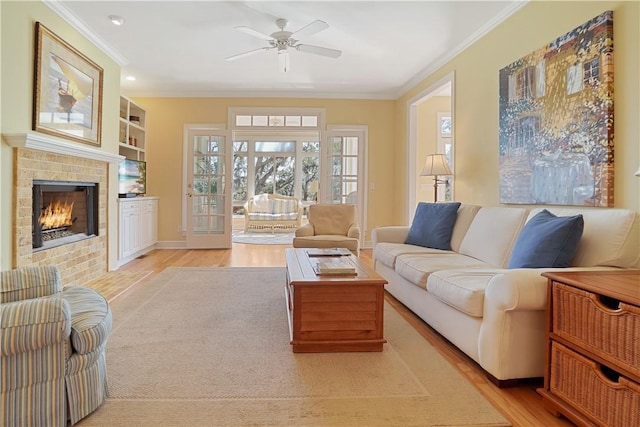 living area featuring a tile fireplace, a ceiling fan, baseboards, ornamental molding, and light wood-type flooring