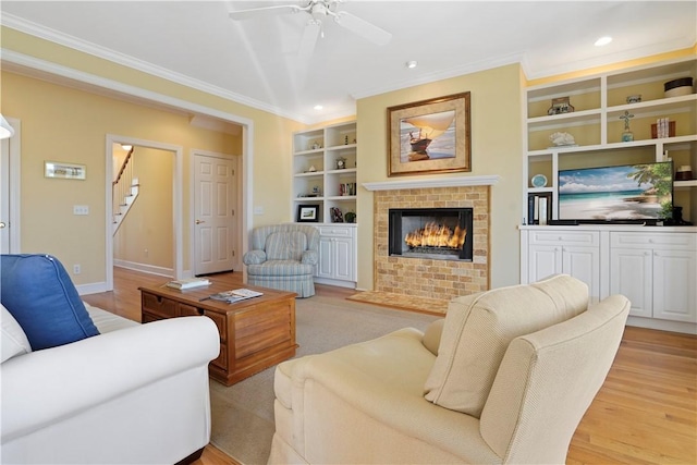 living area with built in shelves, stairs, a brick fireplace, light wood finished floors, and crown molding