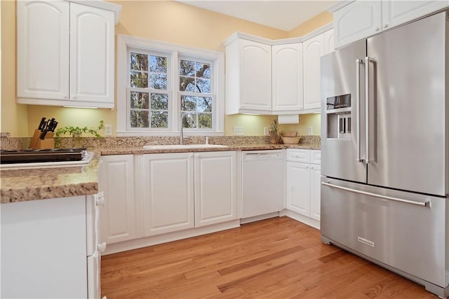 kitchen featuring white cabinets, dishwasher, high end fridge, light wood-style floors, and a sink