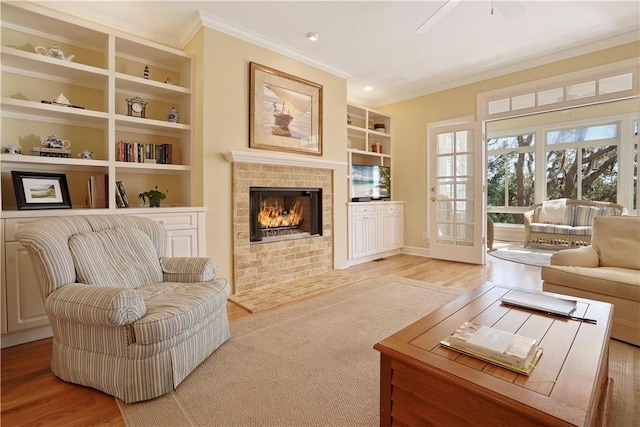 sitting room featuring built in shelves, a fireplace, wood finished floors, a ceiling fan, and ornamental molding