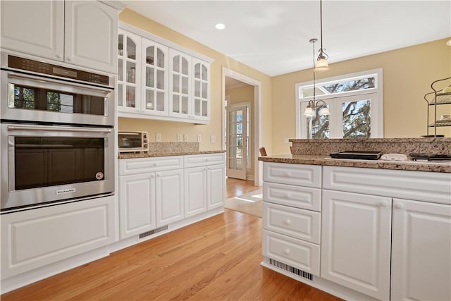 kitchen with light stone counters, visible vents, light wood-style flooring, glass insert cabinets, and stainless steel double oven