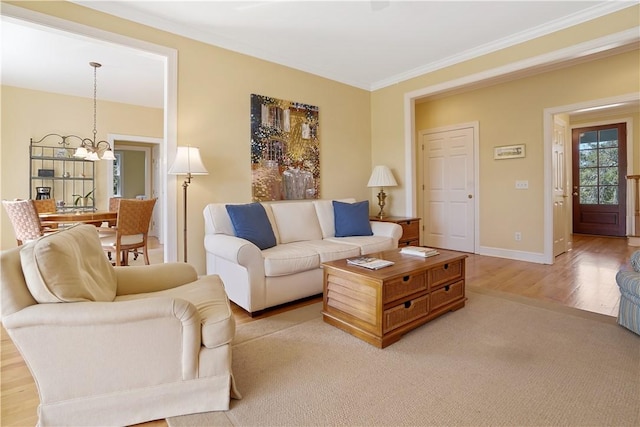 living room featuring light wood-style floors, baseboards, crown molding, and an inviting chandelier