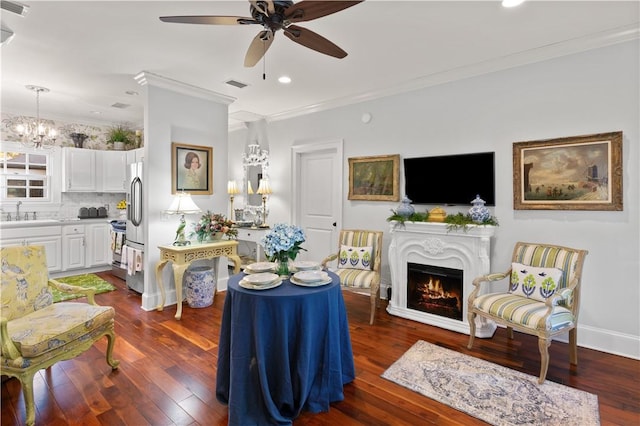 living room with sink, ceiling fan with notable chandelier, crown molding, and dark wood-type flooring