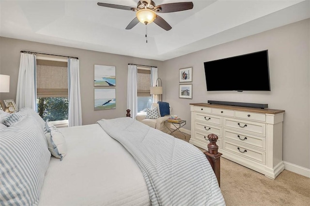 bedroom featuring a tray ceiling, baseboards, light carpet, and ceiling fan