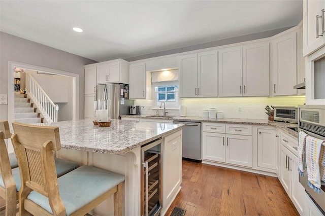 kitchen featuring beverage cooler, a sink, light wood-style floors, appliances with stainless steel finishes, and white cabinetry