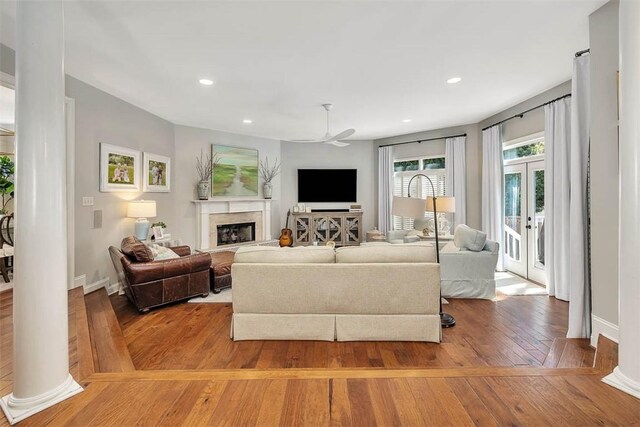 living area with light wood finished floors, ceiling fan, recessed lighting, a glass covered fireplace, and ornate columns