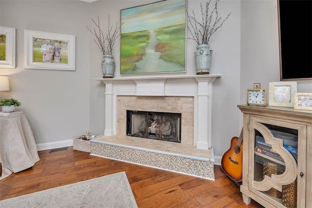 living room with a tiled fireplace, hardwood / wood-style flooring, visible vents, and baseboards