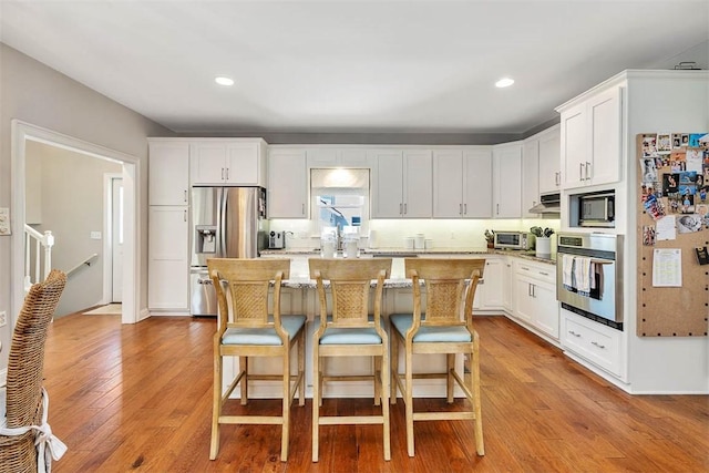 kitchen featuring a center island, a kitchen bar, appliances with stainless steel finishes, wood finished floors, and white cabinetry